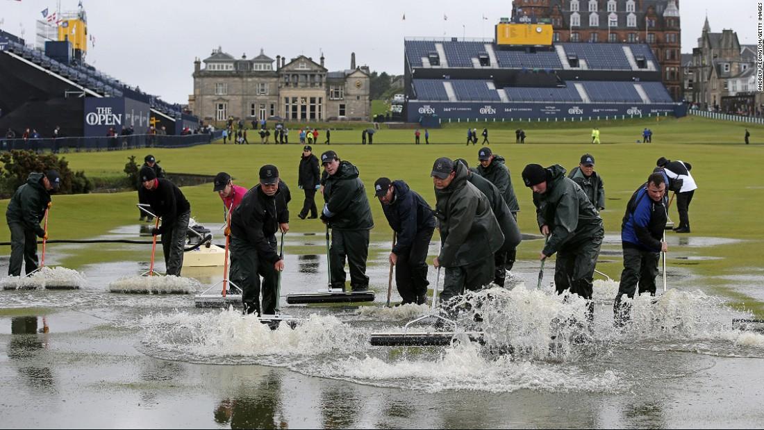 People sweep water off the greens for The Open