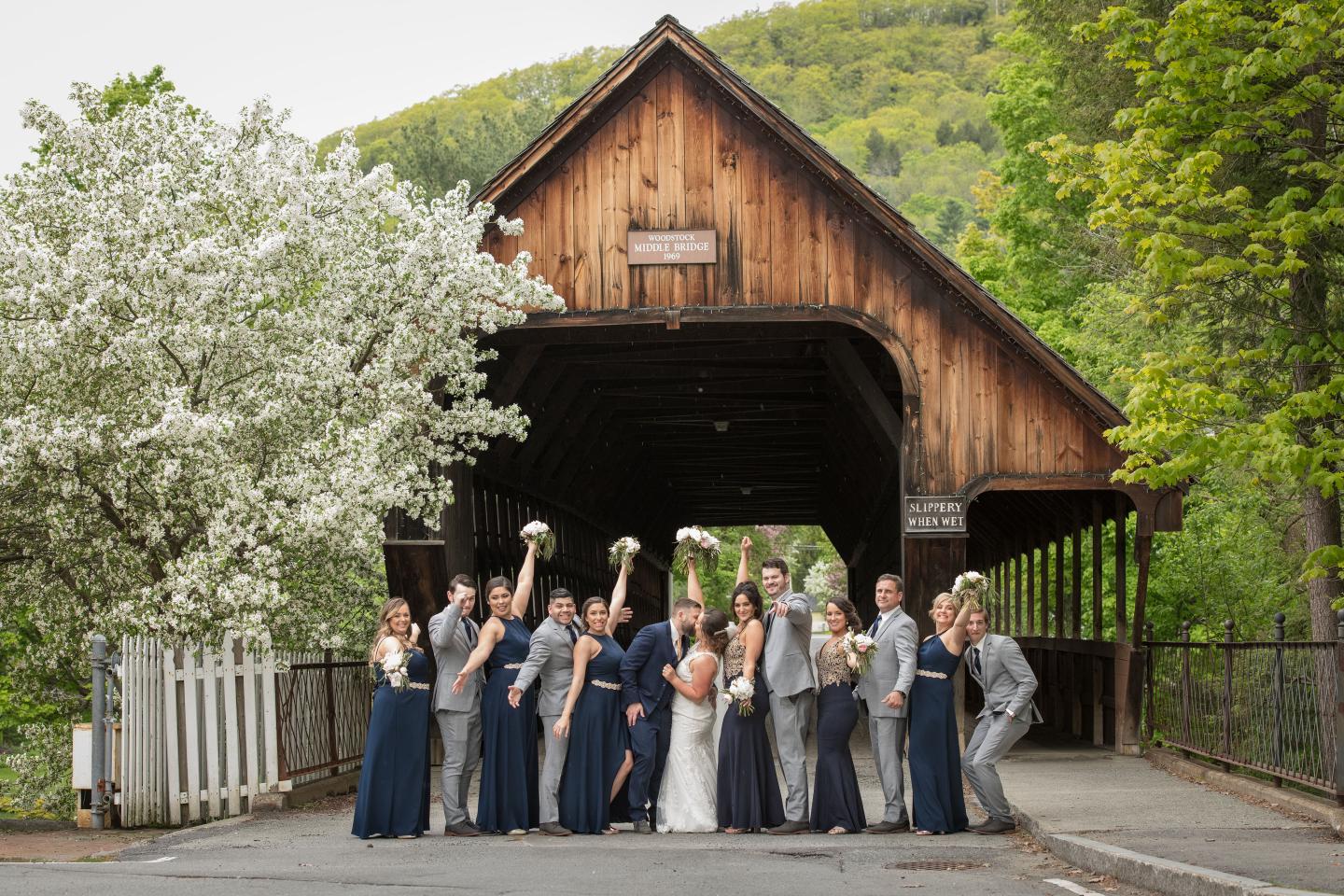 Large bridal party celebrates in front of the covered bridge in Woodstock Vermont with blossoming tree