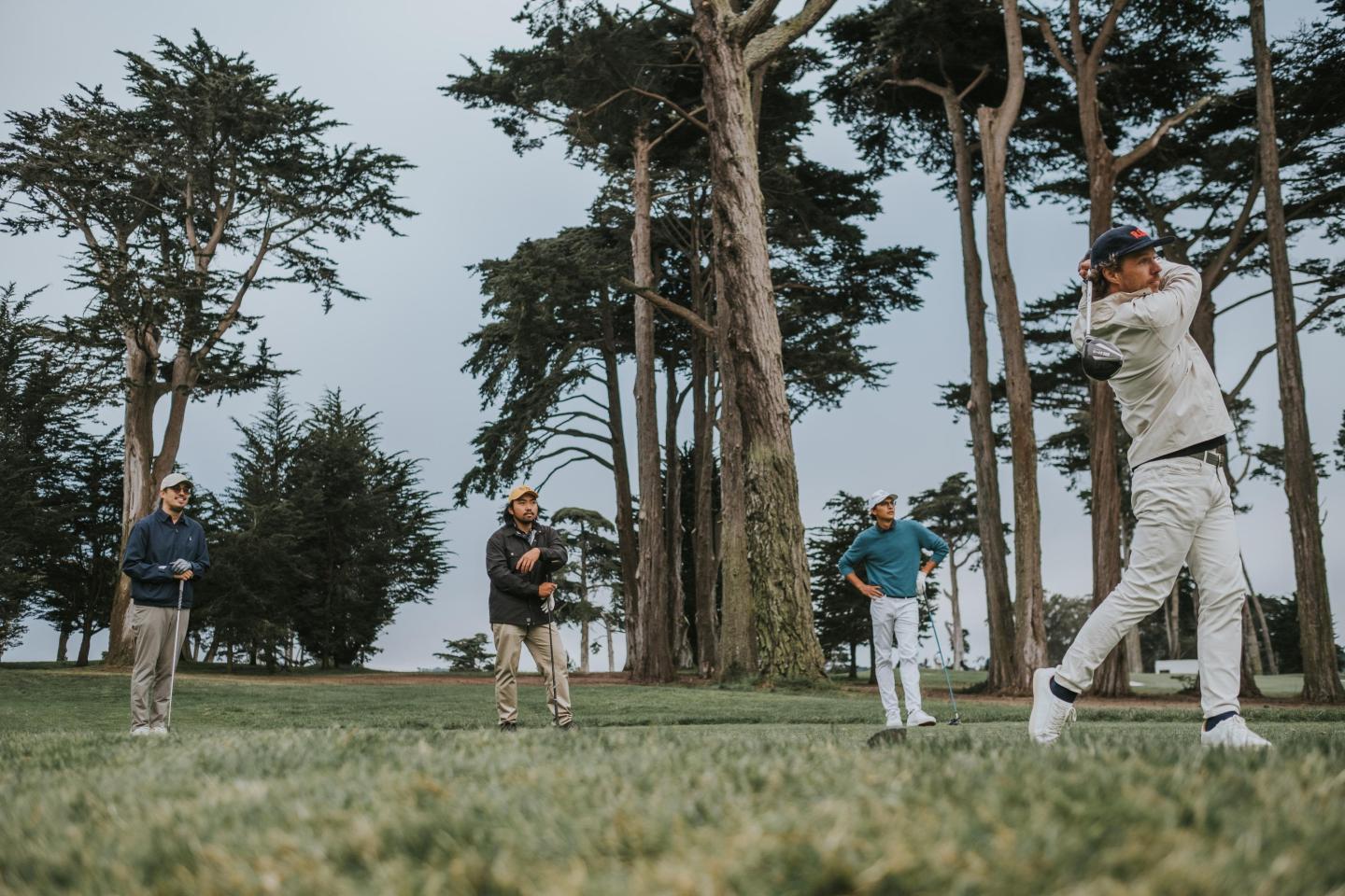 Golfer swings as 3 other golfers look on