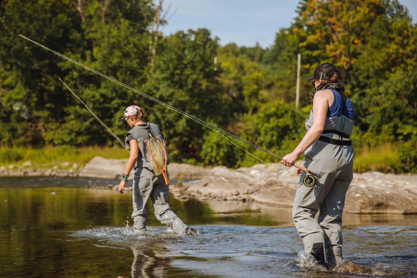 two women wading into the river with fly fishing gear