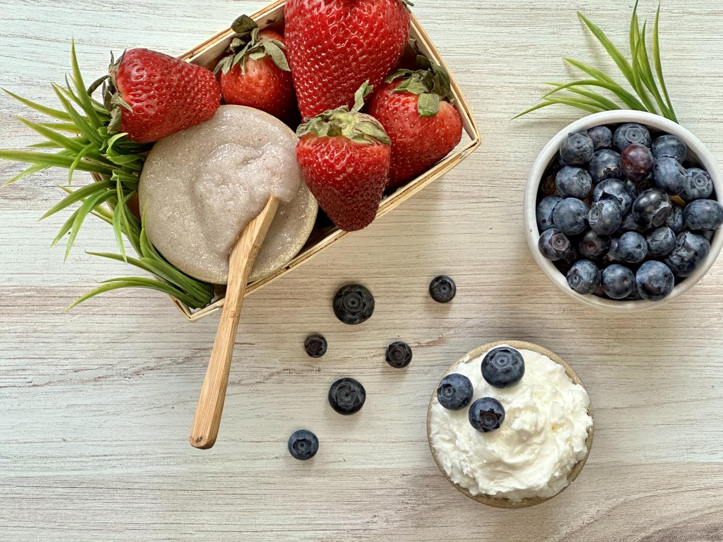 basket of strawberries with a sugar scrub alongside a bowl of blueberries and a small jar of lotion with blueberries in it