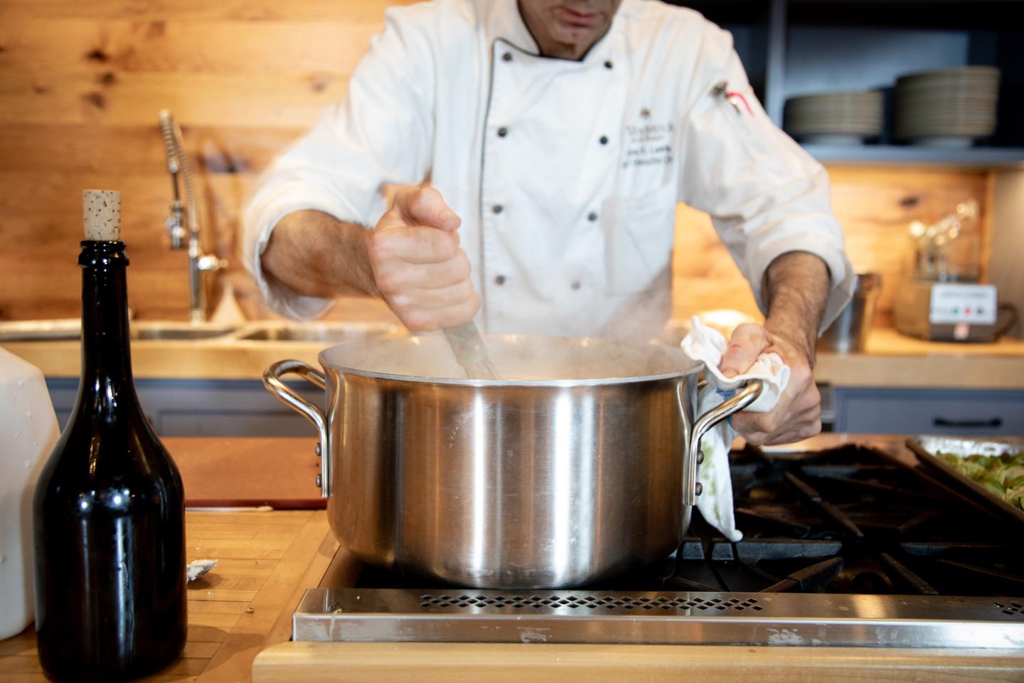 Chef stirring dish in a steaming pot.