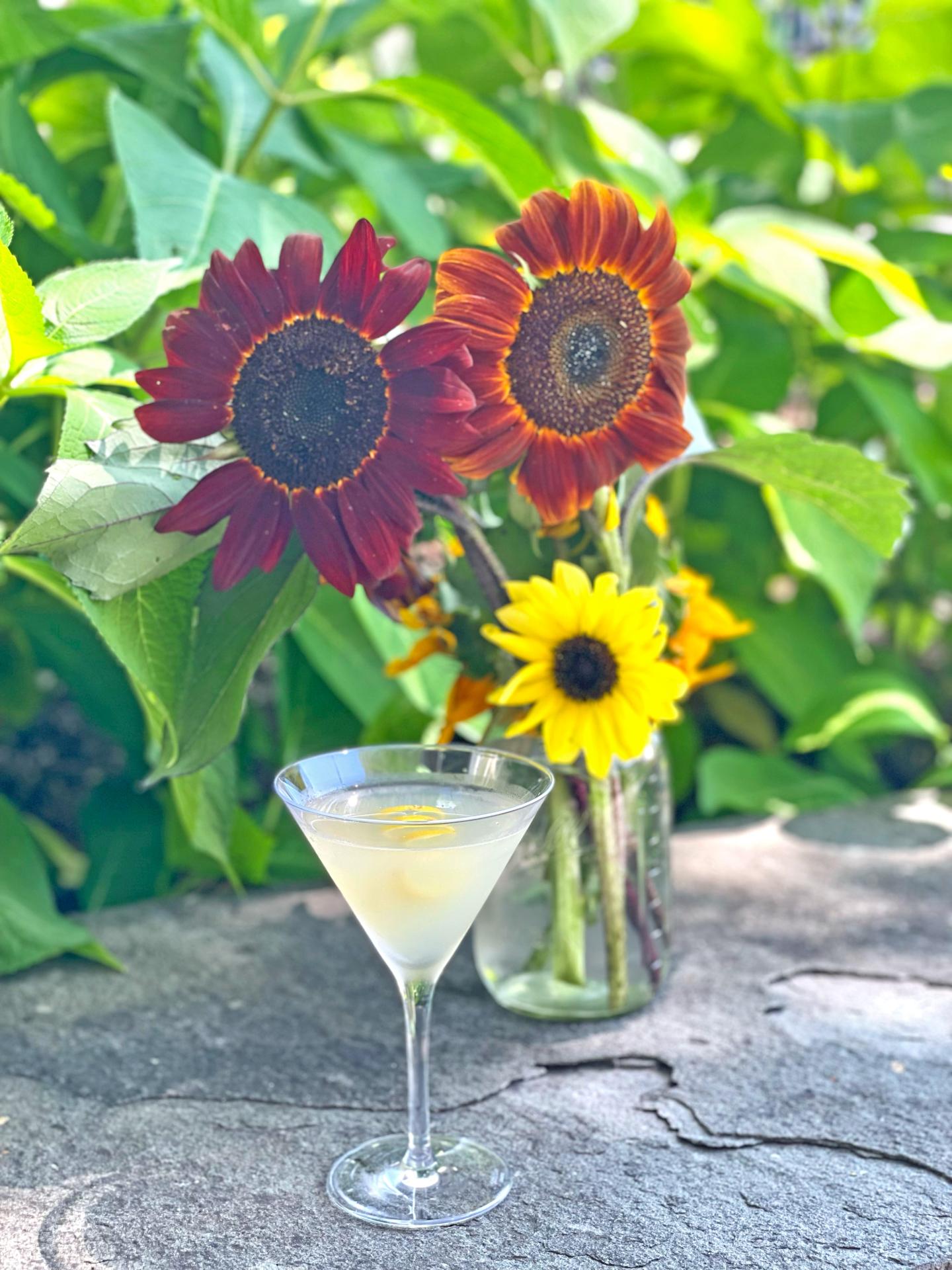Bees Knees cocktail sitting on a rocky surface with red and yellow flowers around the drink