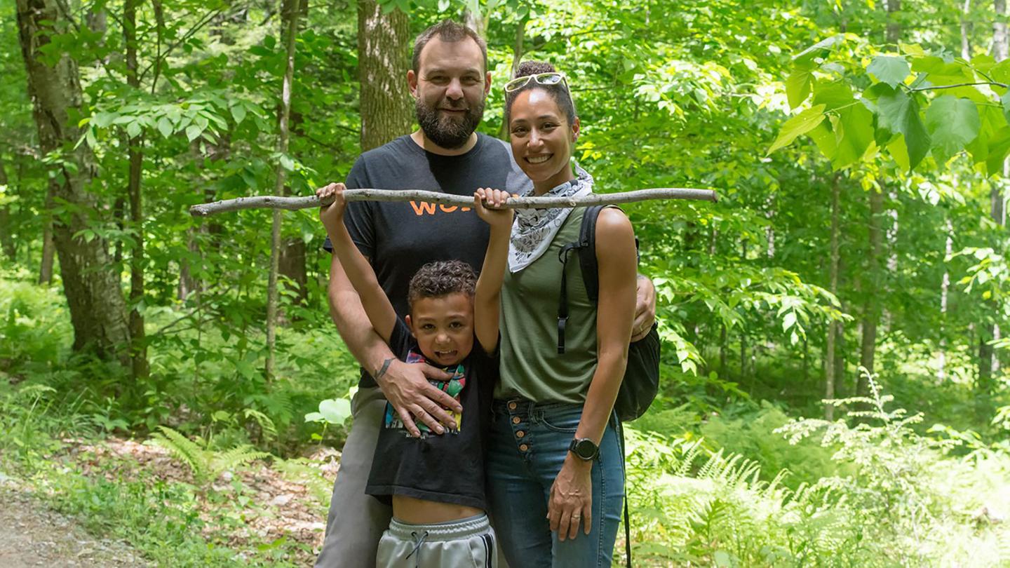 Family enjoying time outdoors. Young boy is holding up a stick while the man and the woman are smiling for the camera.