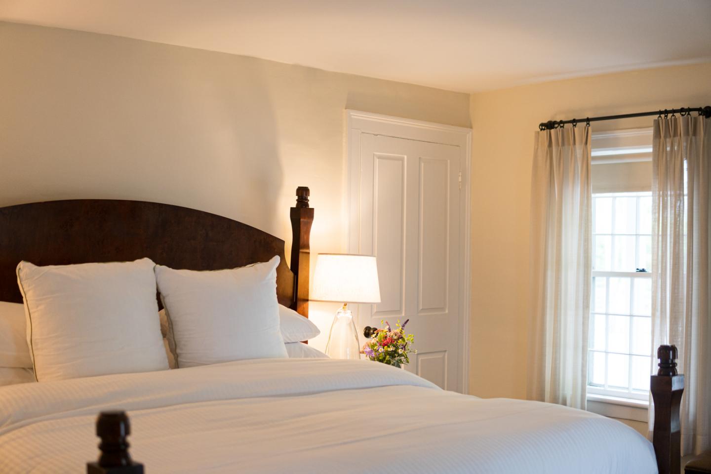 Queen bed with white pillows and sheets. Bedside lamp turned on with colorful arrangement of flowers next to lamp.