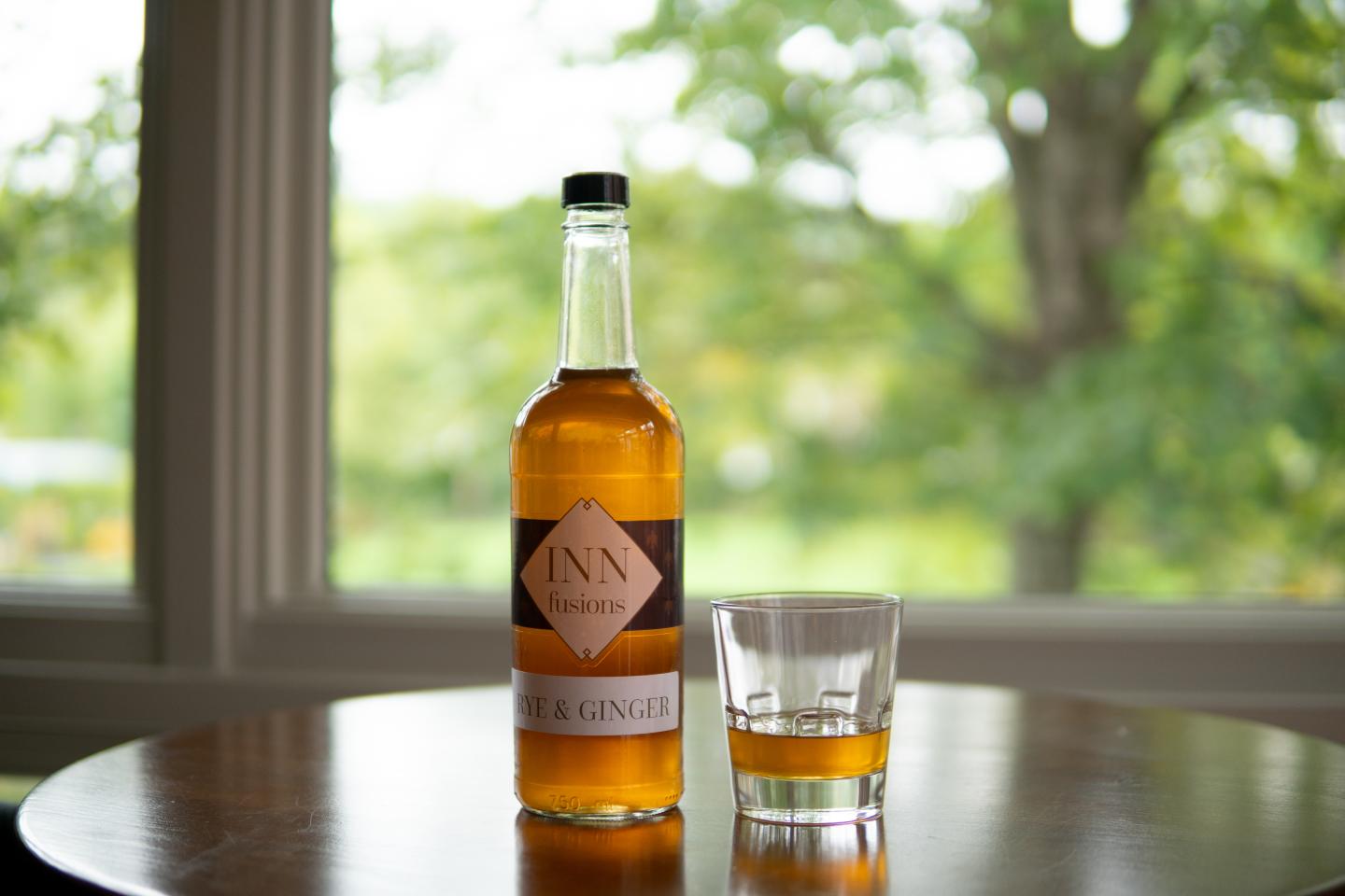 Inn Fusions bottle of whiskey with a glass beside it and green leaves in the background