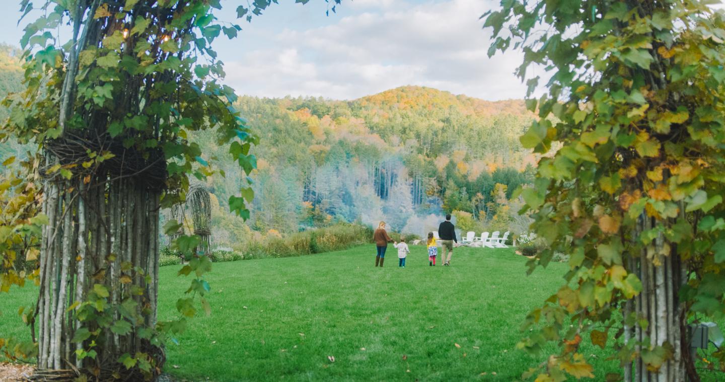 Family walks on the grass event space at Kelly Way Gardens. The hillside behind them is dotted with fall folaige
