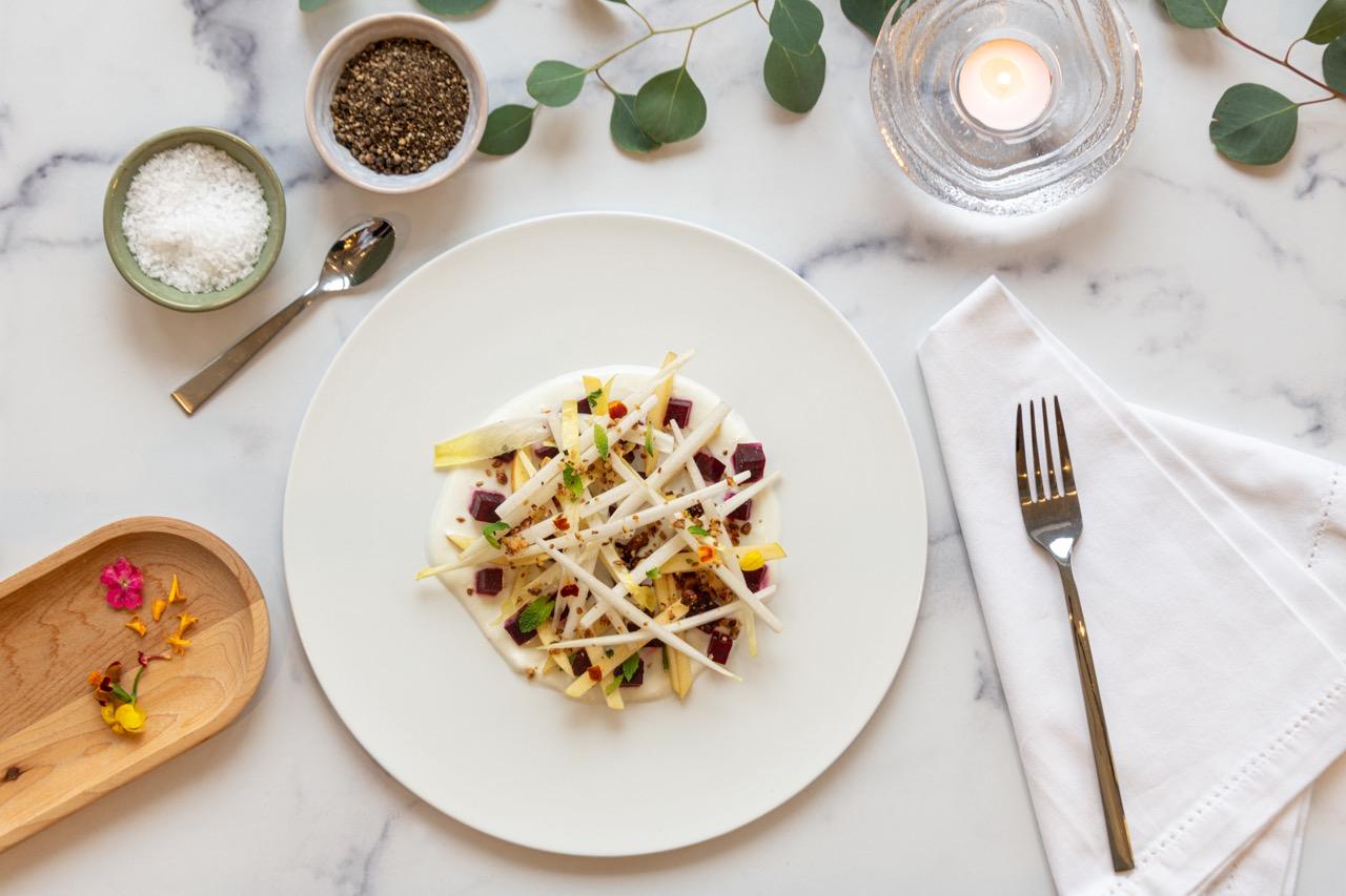 Nicely prepared salad with salt and pepper pinch pots, a fork, and other details surrounding the plate