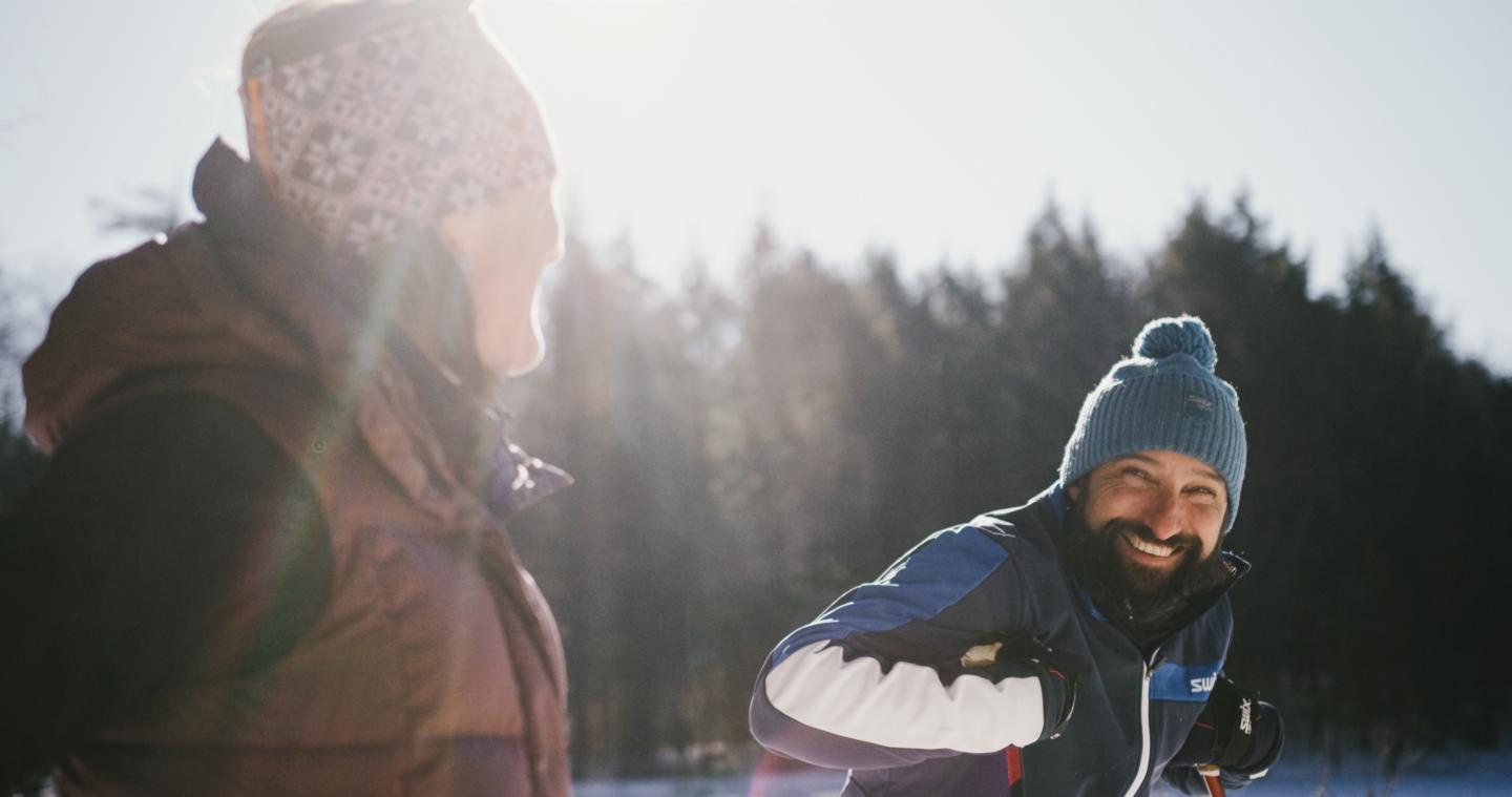 Two people in snow gear laughing and smiling outside in the sun.