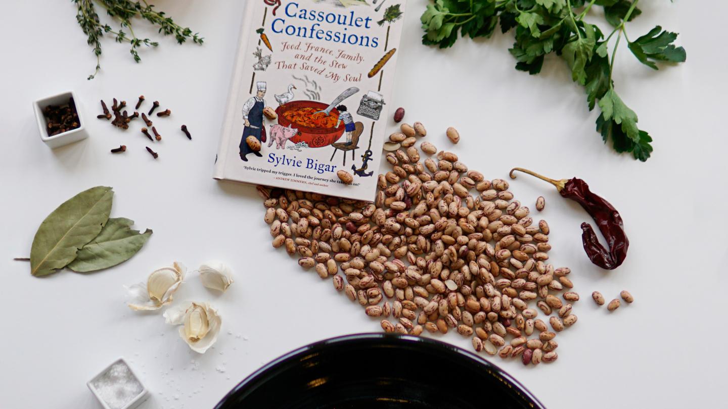 Flatlay of Cassoulet ingredients, including beans, parsley, peppers, bay leaves and more.