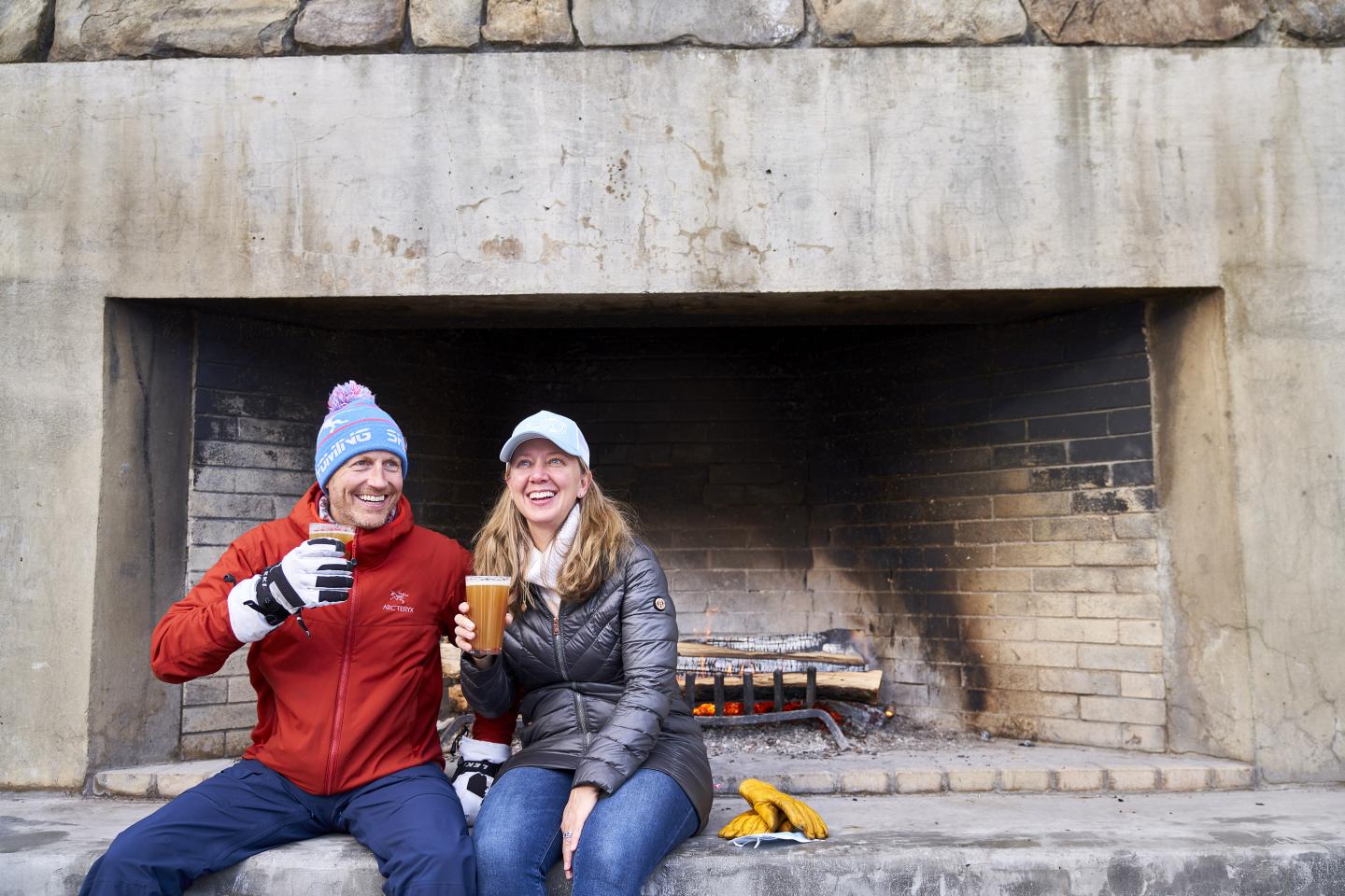 Couple drinking beer by Saskadena Six outdoor fireplace