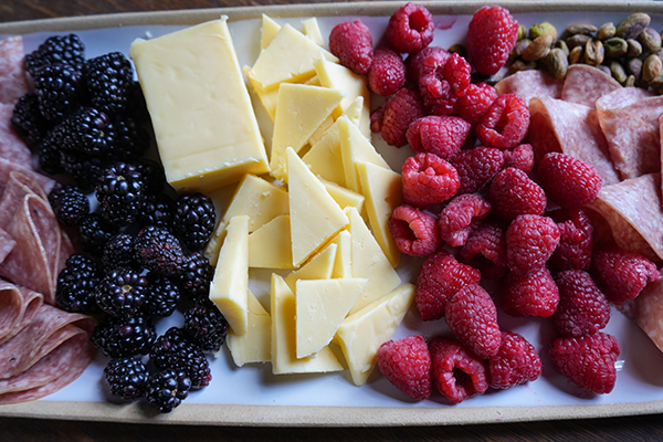 Cheese, blackberries, raspberries, salami, and nuts on a platter.