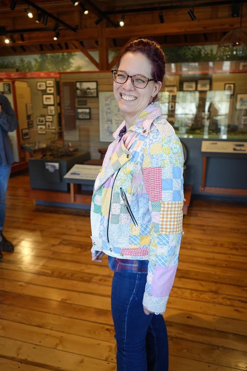 Smiling person in a colorful patchwork jacket stands in a museum.