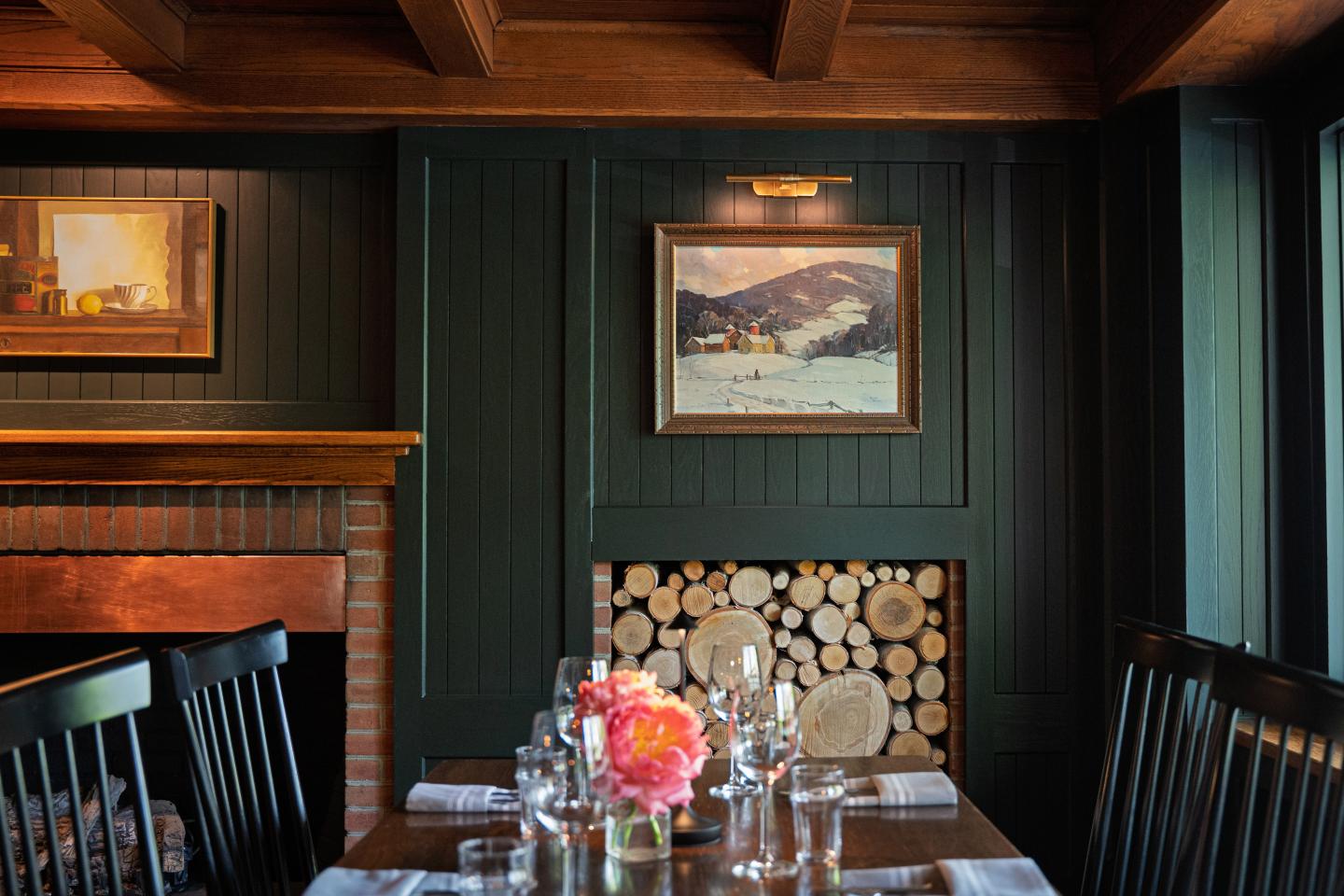 Cozy dining area with dark wood, paintings, and set table with flowers.