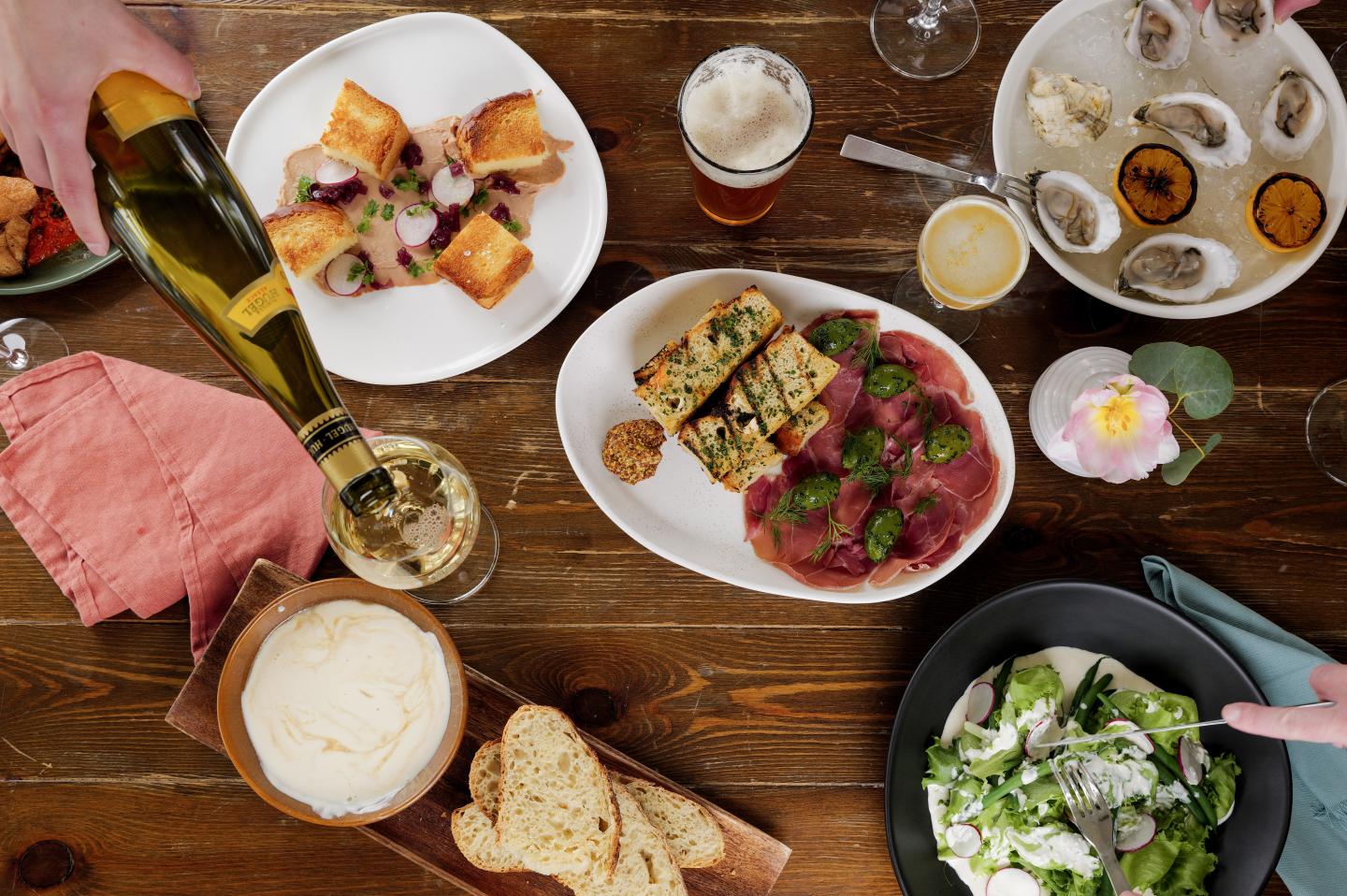 A selection of dishes on a wooden table, with wine being poured into a glass.