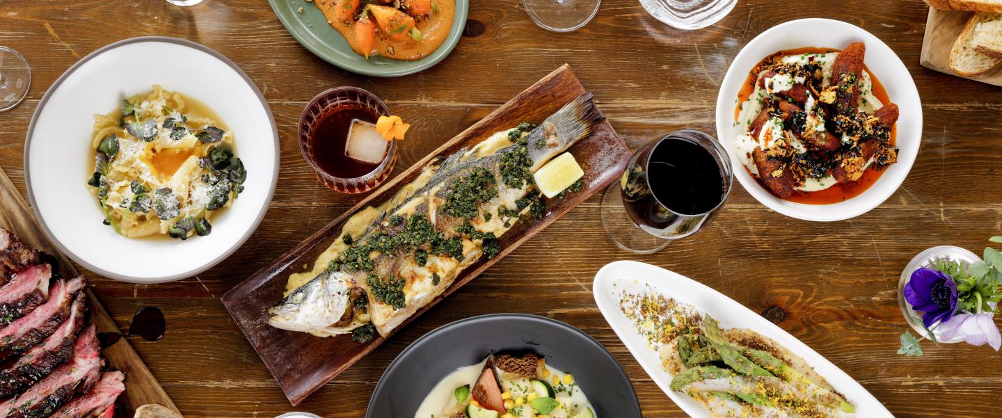 Assorted gourmet dishes on a wooden table with wine and water glasses.