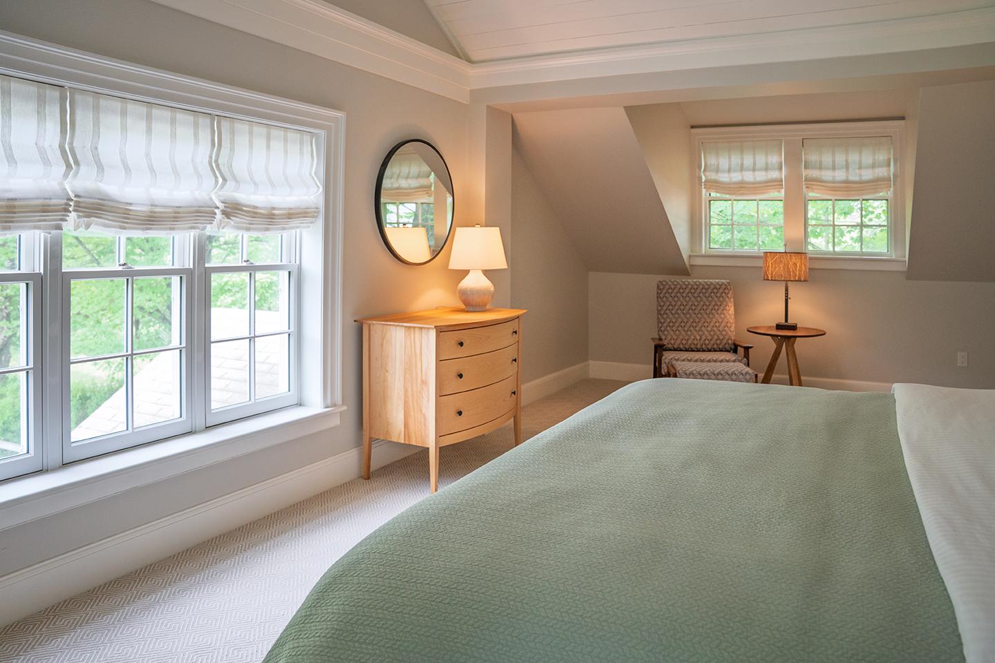 Cozy bedroom with green bedspread, large window, dresser, and lamp.