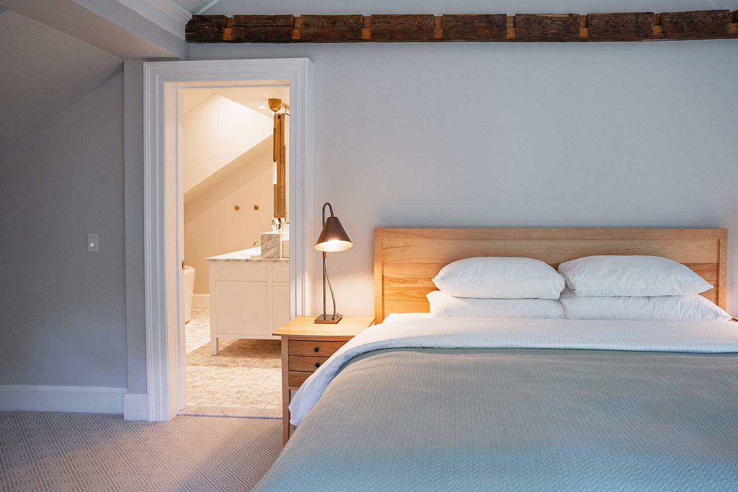 Cozy bedroom with a made bed, lit lamp, and an open door to a bathroom.