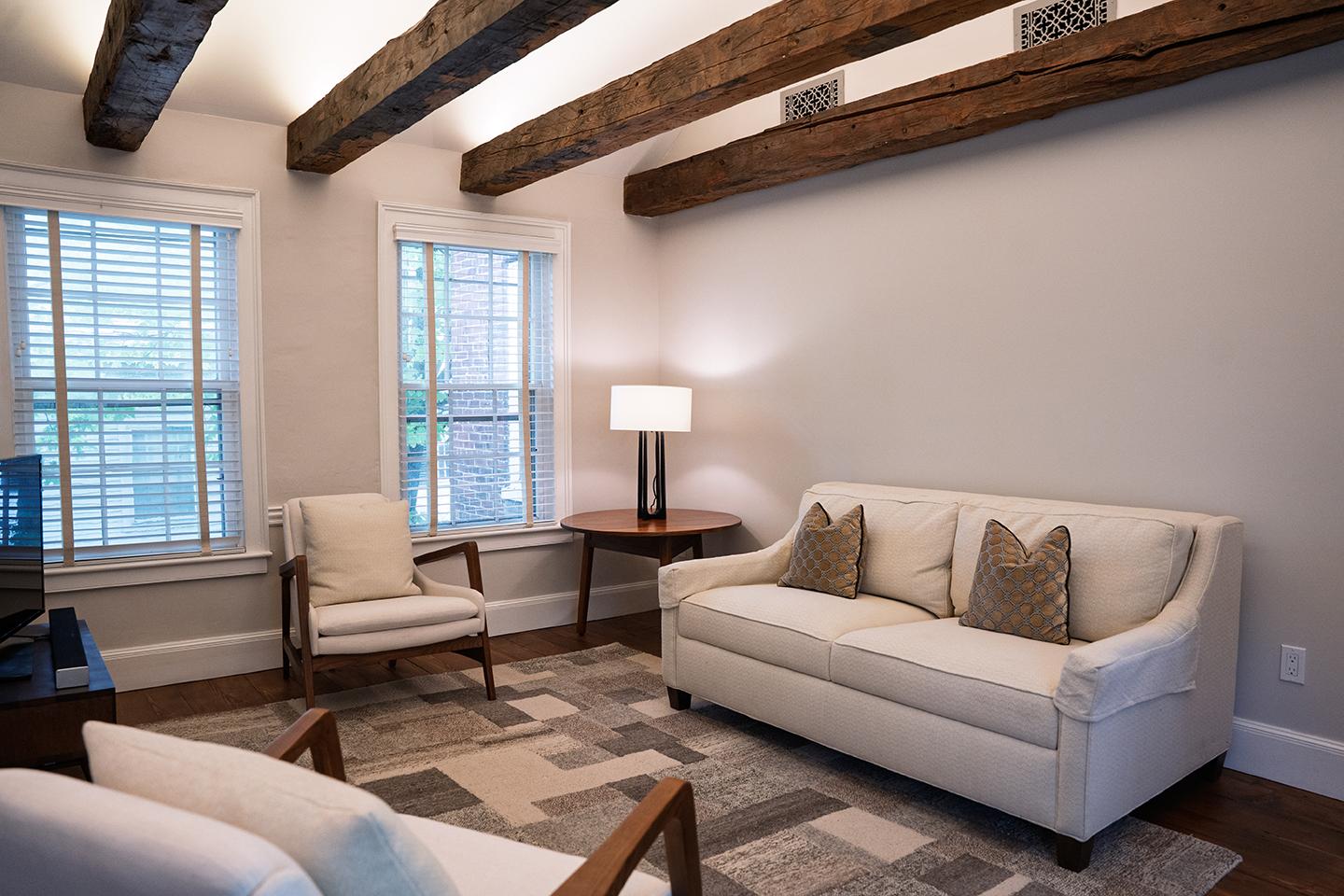 Cozy living room with white sofa, armchair, and wooden beams.