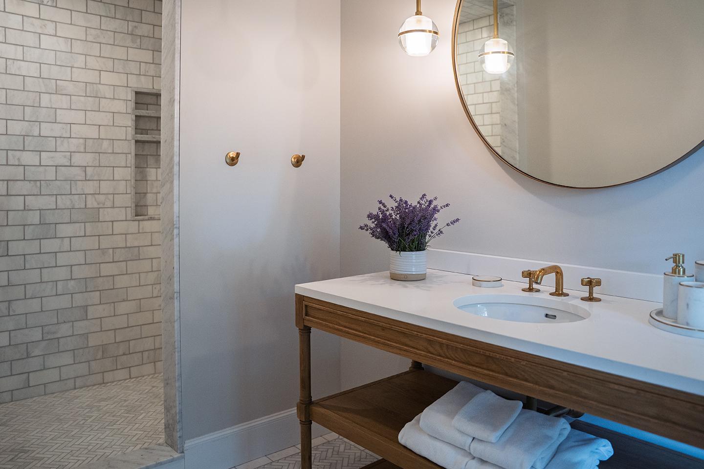 Elegant bathroom with a round mirror, sink, lavender vase, and shower area.