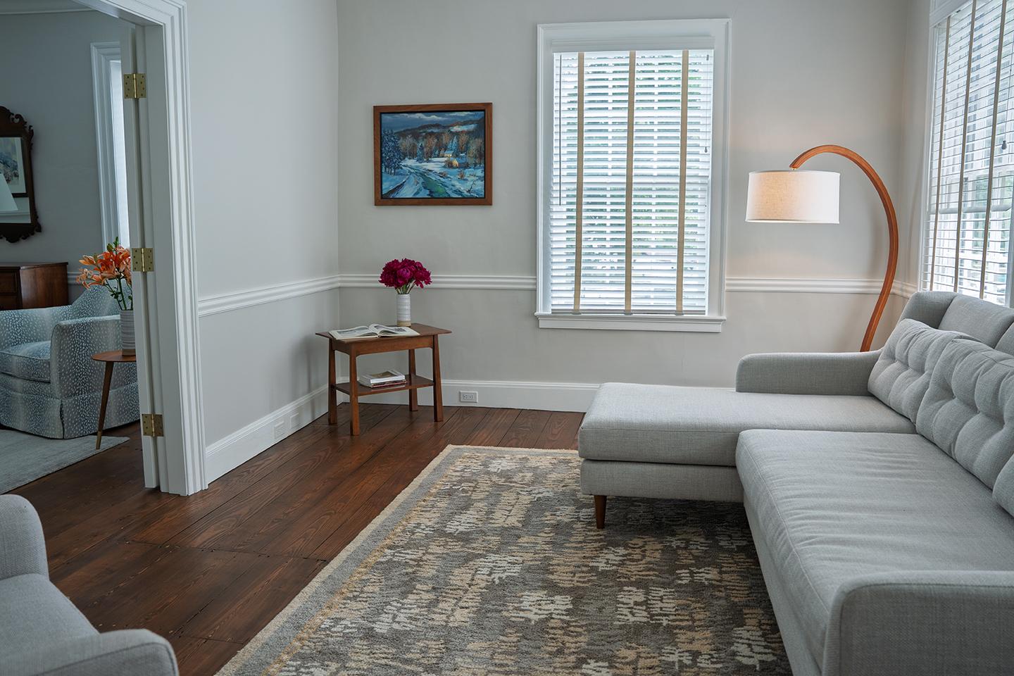 Bright living room with a gray sofa, wooden floor, and a lamp by the window.