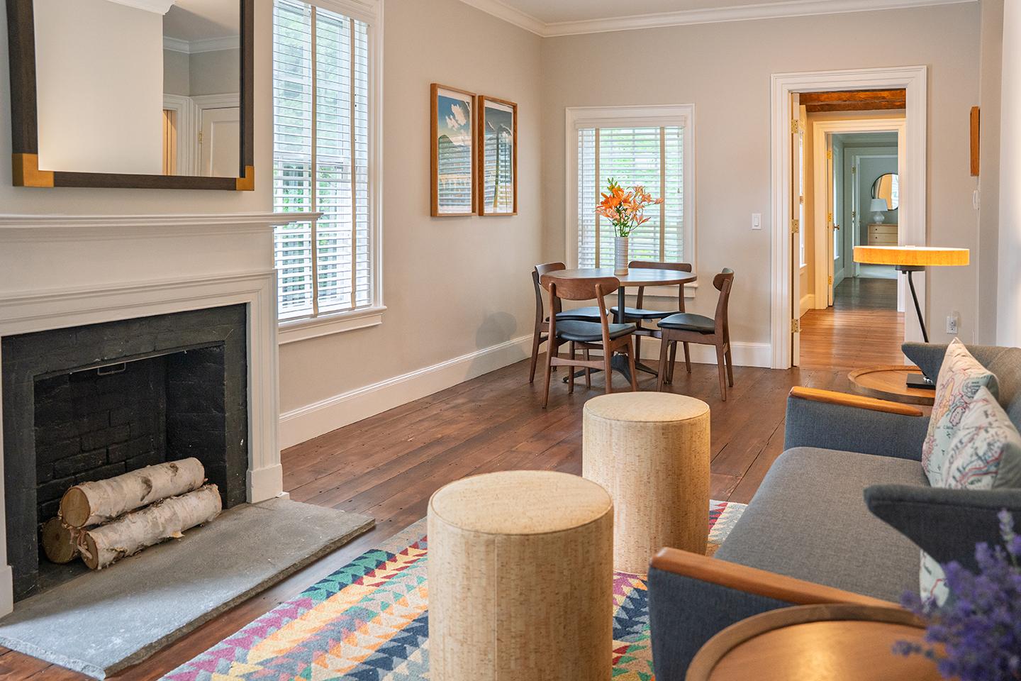 Cozy living room with fireplace, colorful rug, and dining area in the background.