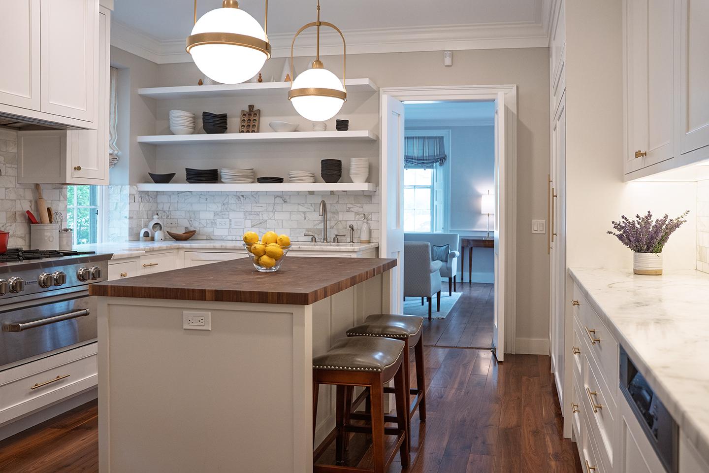 Modern kitchen with island, stools, and pendant lights. Marble backsplash and wooden floor.