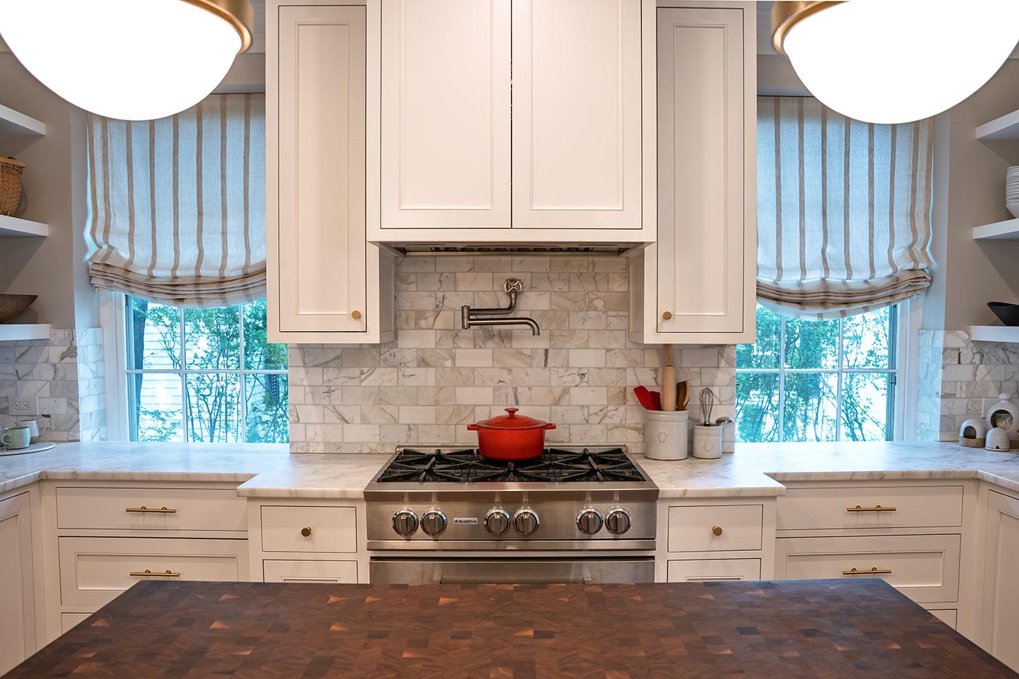 Bright kitchen with white cabinets, a red pot on the stove, and striped curtains.