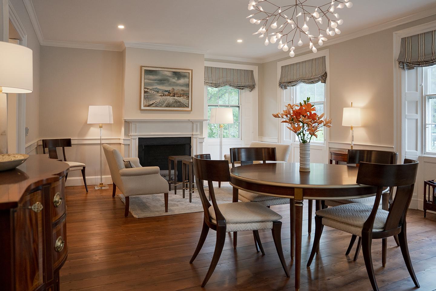 Elegant dining room with round table, modern chandelier, and vase of orange flowers.