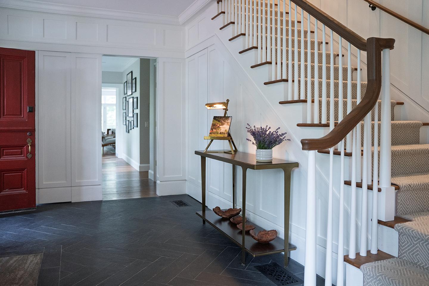 Hallway with red door, staircase, and table with flowers and books.