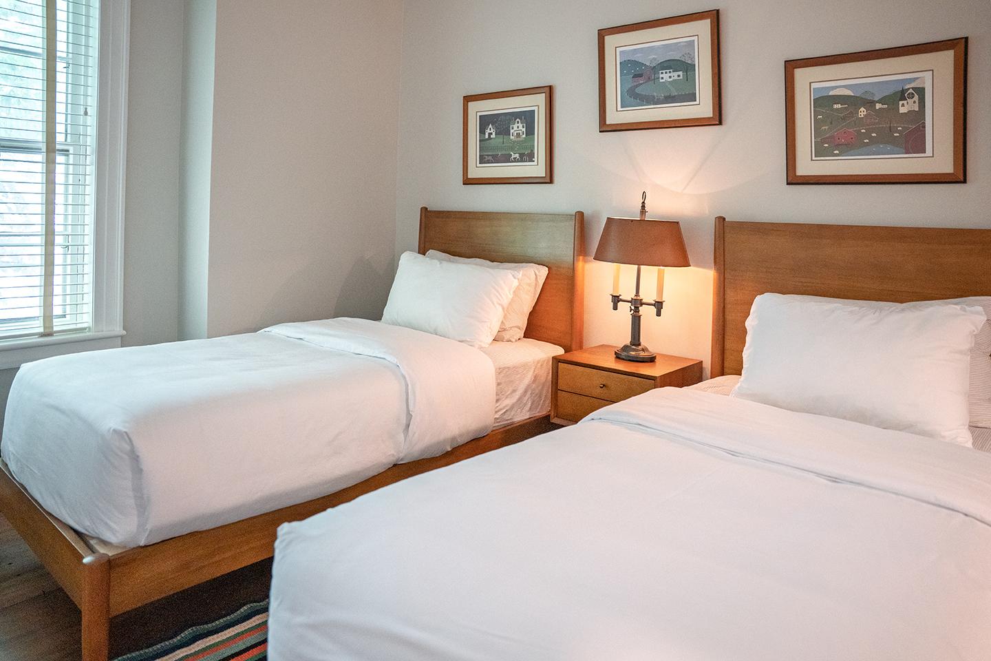 Two neatly made twin beds with white bedding in a cozy, light-filled room.