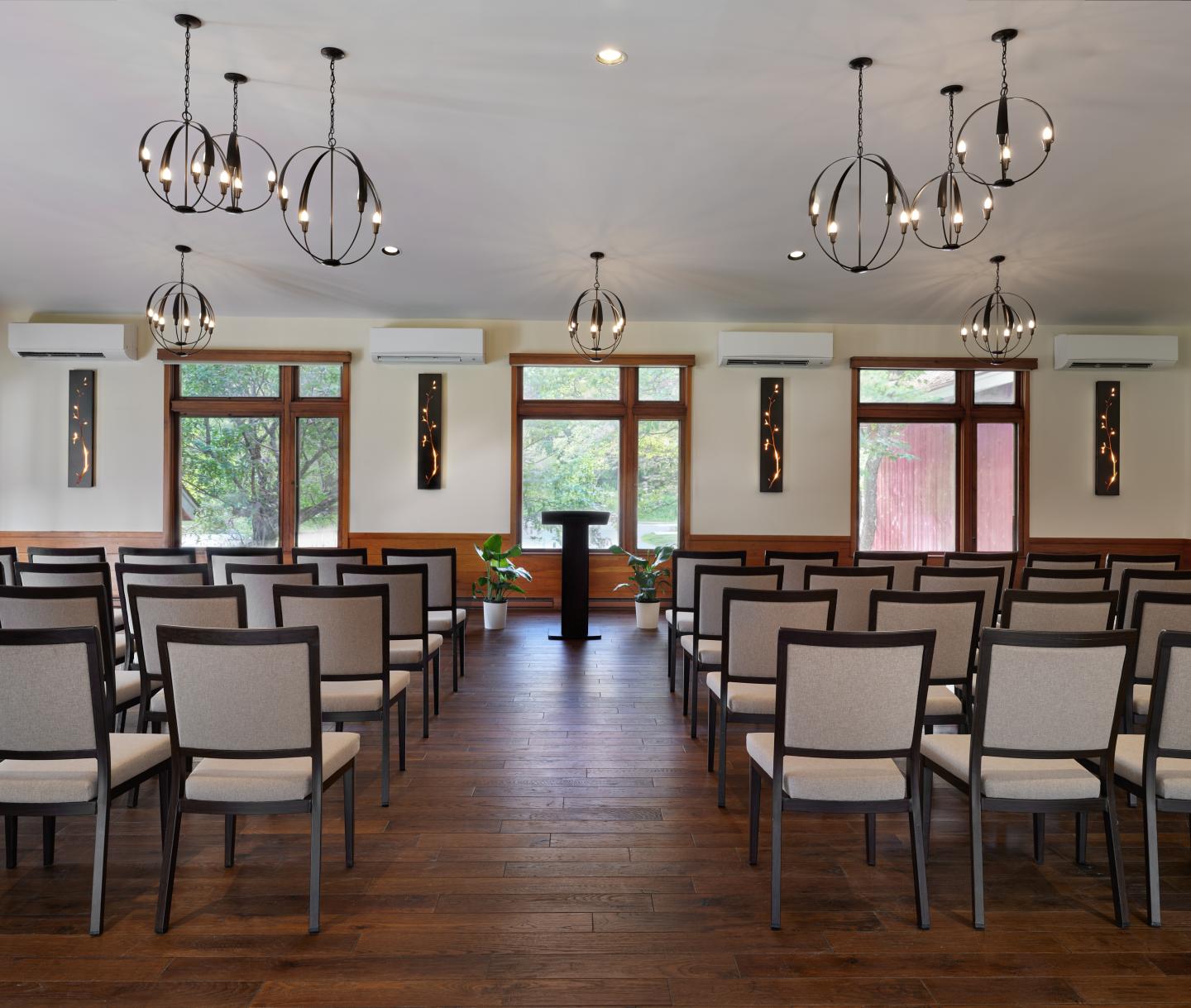Quiet conference room with rows of chairs facing a podium, large windows, modern lighting.