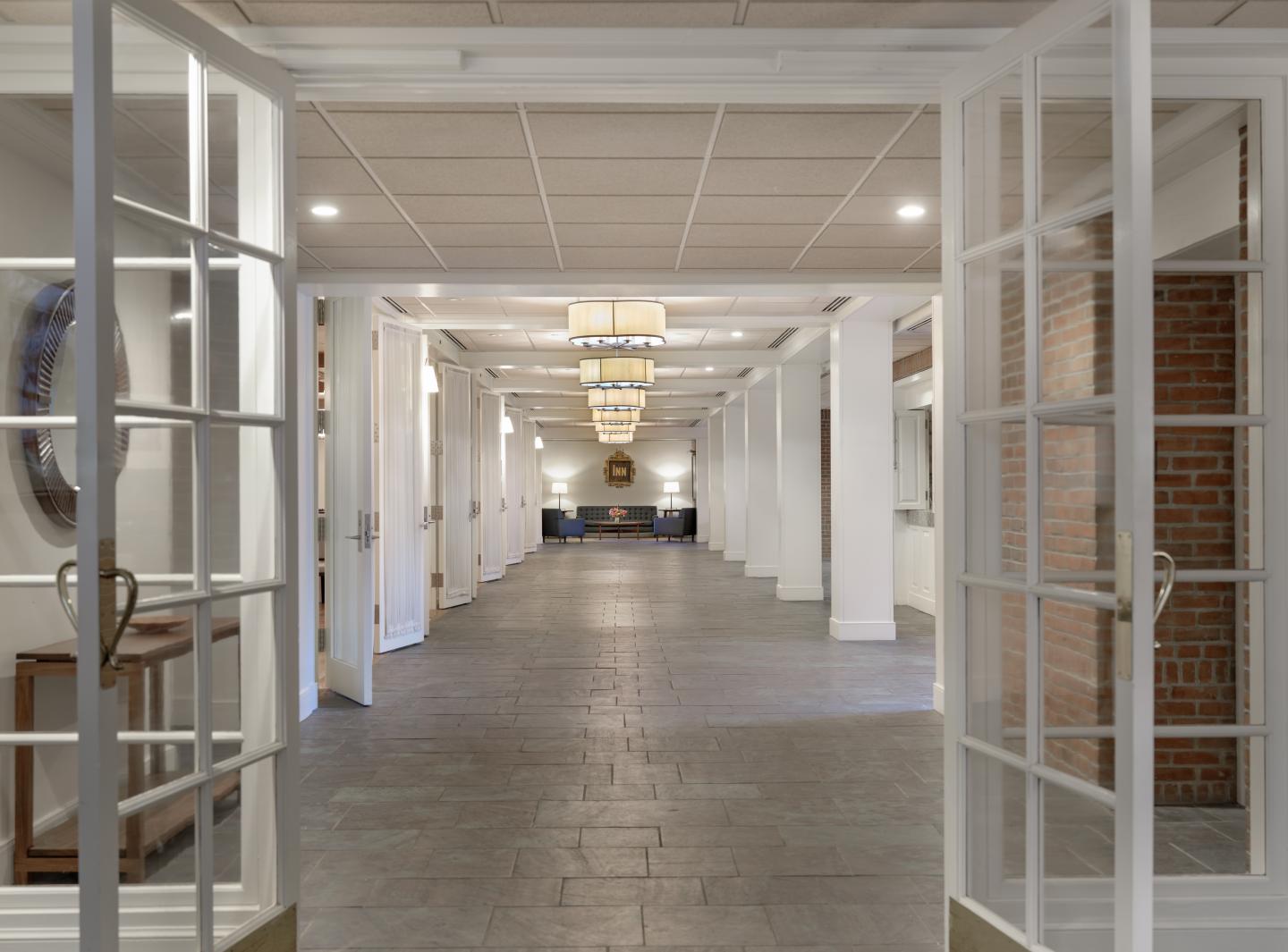 Wide hallway with open double doors, brick walls, and ceiling lights.