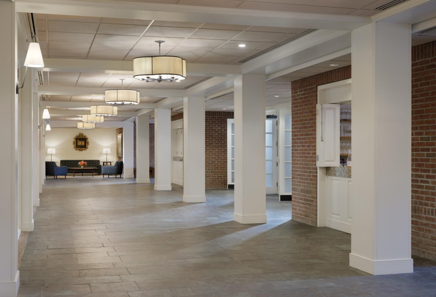 Bright, spacious hallway with pillars and hanging lamps. Brick wall on the right side.