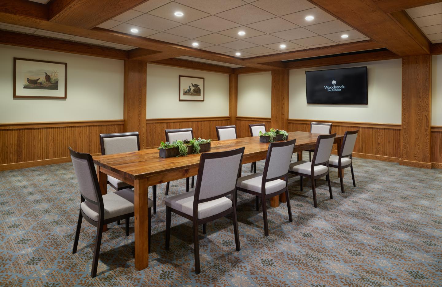 Meeting room with a long wooden table, several chairs, and framed artwork on the walls.