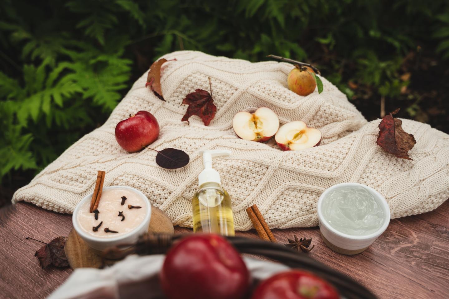 Cozy autumn setup with apples, cinnamon, and skincare products on a blanket.