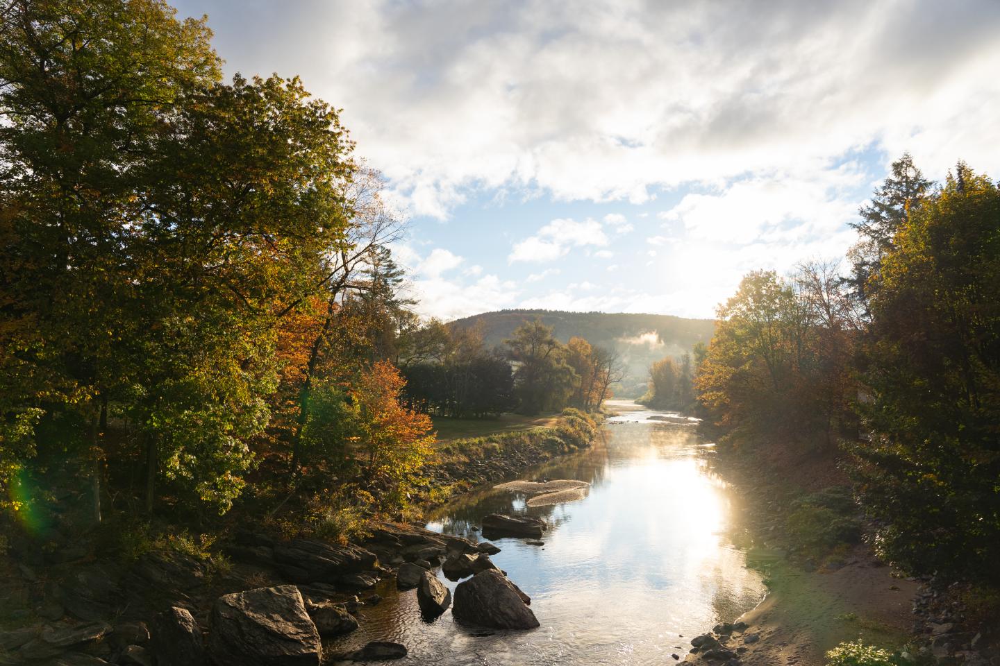 River flowing through autumn trees under a cloudy sky.