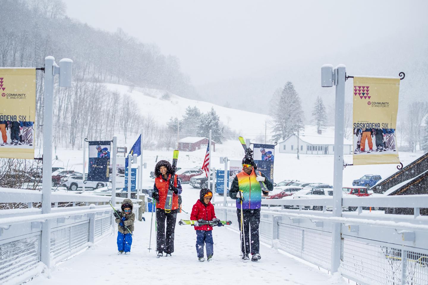 Family dressed in winter attire walking on snowy path in a ski resort.