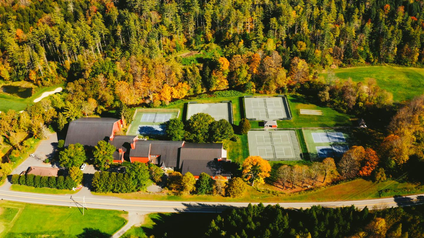 Tennis courts and buildings surrounded by autumn trees, viewed from above.