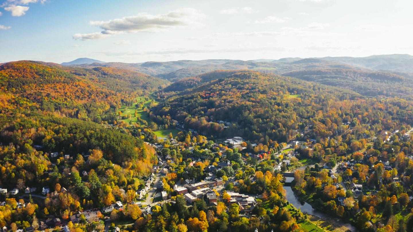 Aerial view of a town surrounded by autumn hills and trees.