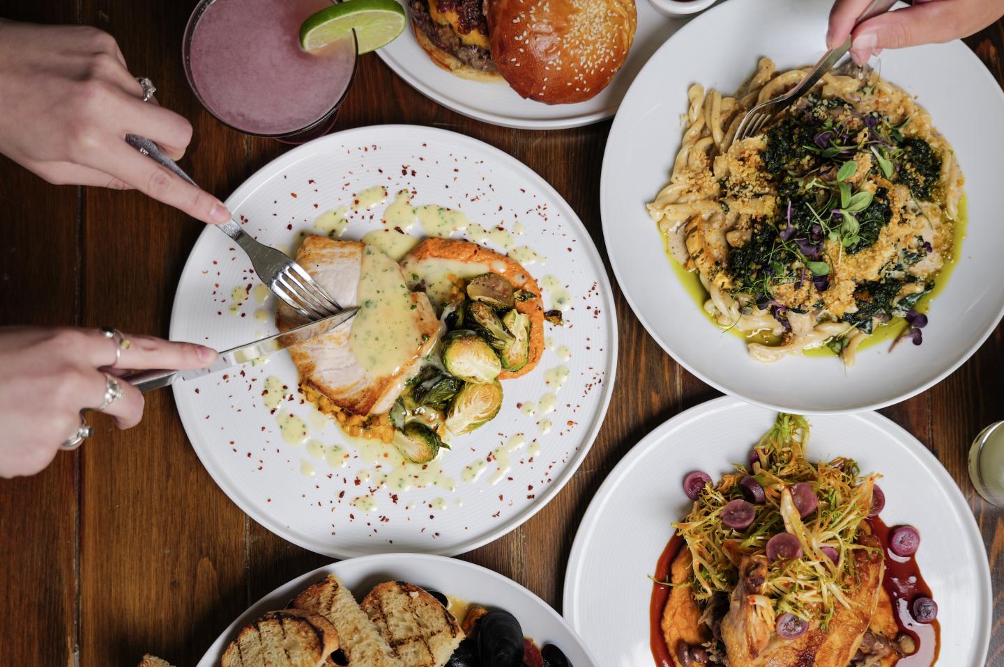 Hands cutting a meal on a table with various dishes, including pasta and salads.