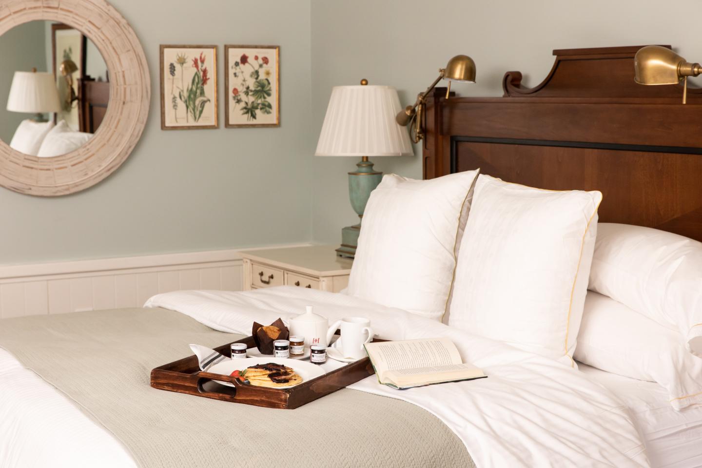 Cozy bedroom with a tray of breakfast and open book on the bed.