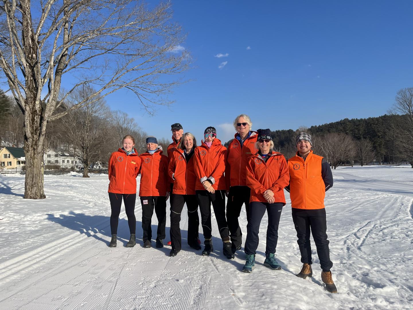 Group in orange jackets standing on snowy field under clear blue sky.
