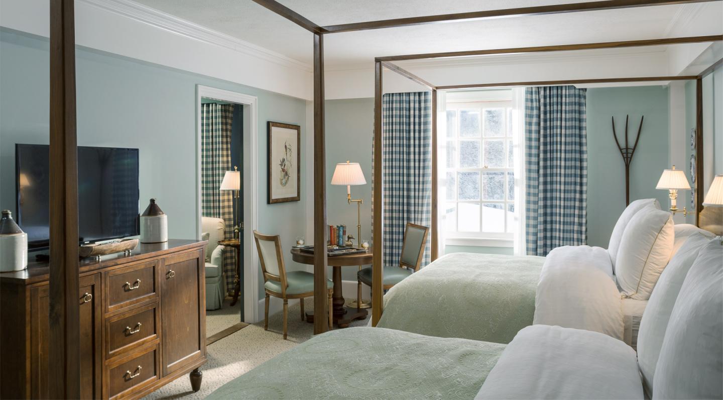 Hotel room with two canopy beds, a dresser, TV, and a window with blue curtains.