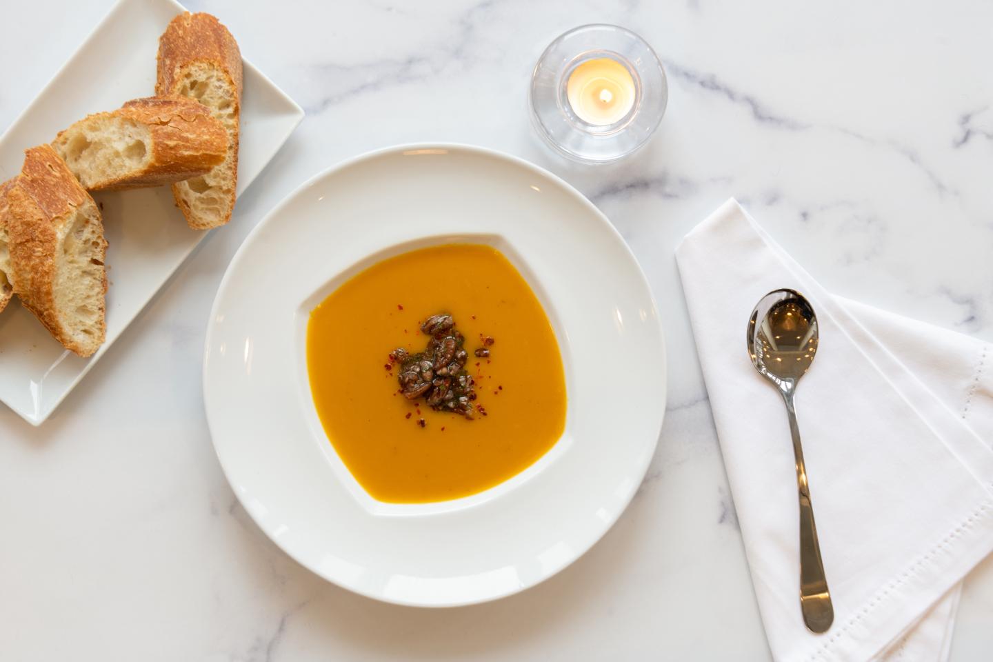 Soup with garnish, bread on a plate, spoon and napkin on marble table.