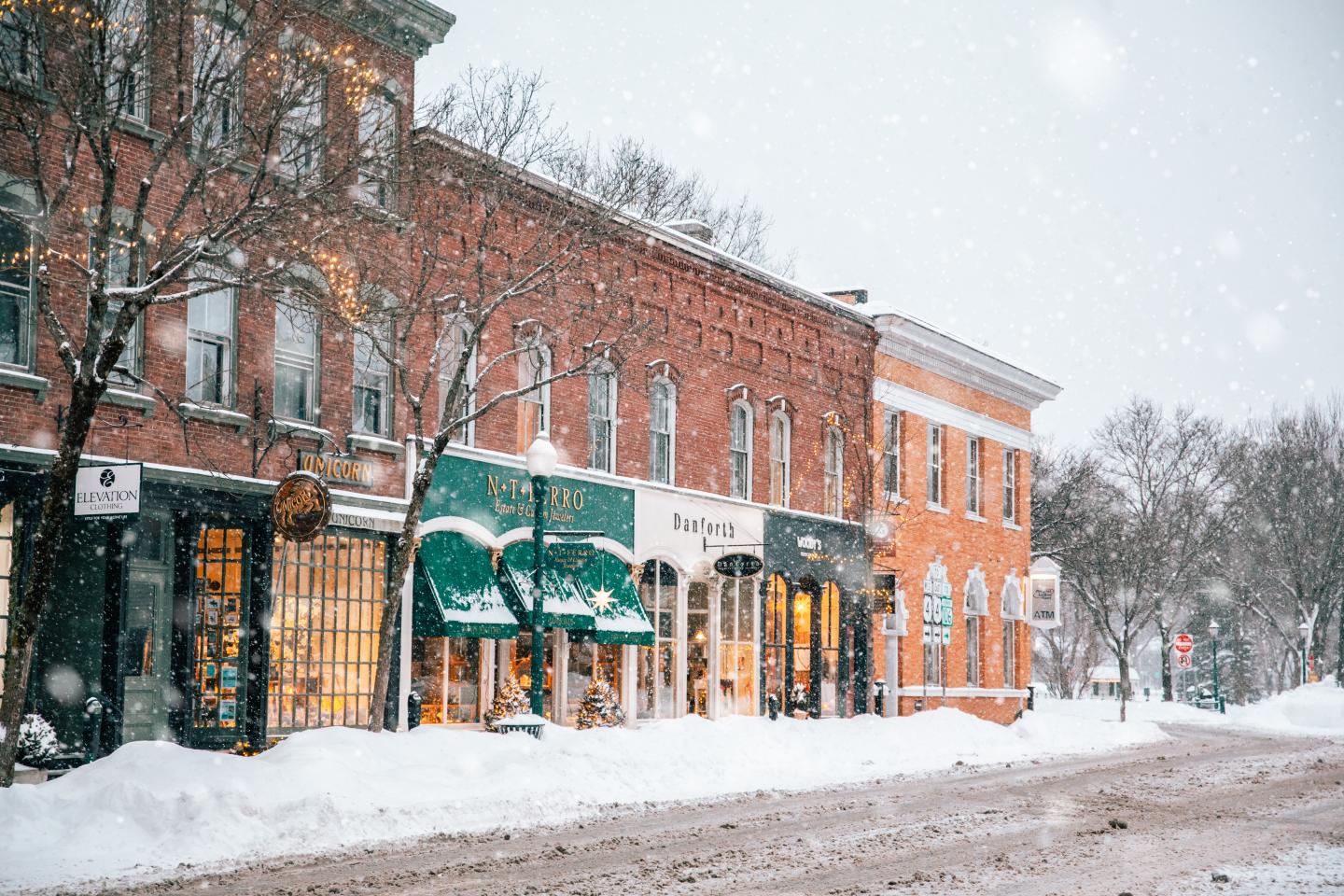 Snowy street with colorful brick buildings and falling snowflakes.