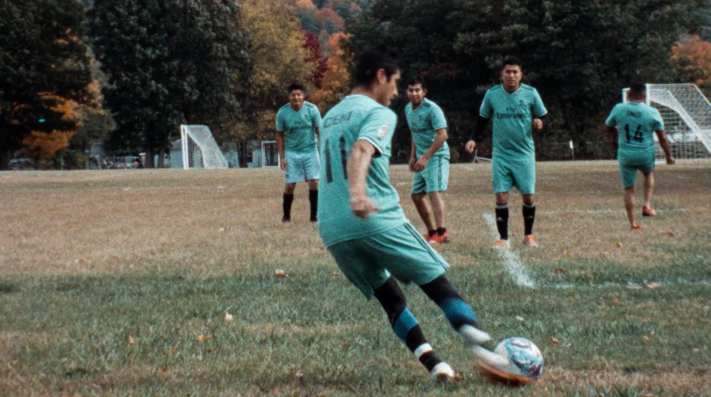 Soccer player kicking ball on grassy field with teammates in the background.