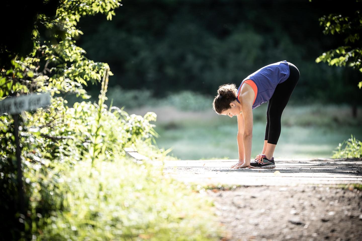 Woman stretching outdoors in sunlight on a forest path.