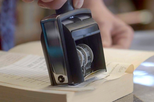 Date stamp on a library book page, hand holding the stamp.