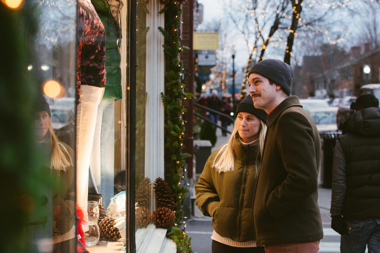 Couple window-shopping on a snowy street, dressed warmly.